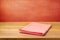 Empty wooden table with checked tablecloth over grunge red concrete wall.