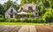 An empty wooden table in the foreground, with a blurred country house in the background against a verdant garden setting