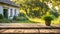 An empty wooden table in the foreground, with a blurred country house in the background against a verdant garden setting