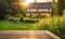 An empty wooden table in the foreground, with a blurred country house in the background against a verdant garden setting