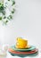 Empty yellow cups and brightly colored plates on a white table covered with a linen tablecloth, a flower pot on the wall in the