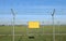 Empty yellow sign outside a double wire mesh barrier with barbed wire on top.