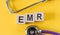 EMR - electronic medical record acronym, building from wooden cubes on yellow desk with stethoscope