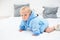 en month blond baby boy crawling on bed in blue bathrobe. White pillows in background. Baby care concept, banner copy space
