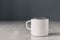 Enamel white metal mug with black line on the edge on white wooden table on gray background. Place for text or advertising