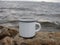 Enamel white mug with coffee on a natural background of the river close-up. minimalism