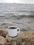 Enamel white mug with coffee on a natural background of the river close-up. minimalism