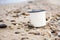 Enameled tourist mug on the sandy beach of Lake Baikal in the summer.