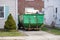 The end of an old blue green dumpster filled with construction debris in a driveway between two houses