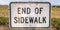 End of Sidewalk sign in front of a grassy terrain