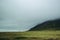 Endless landscapes of Iceland. Pale green grass and misty mountains under gray rainy cloud