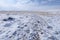 Endless snow-covered steppe under a cloudy sky. Dry plants stick out from under the snow. Snowy mountains on the horizon