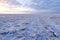 Endless snow-covered steppe under a cloudy sky. Dry plants stick out from under the snow. Snowy mountains on the horizon