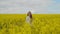 An energetic female singer with a microphone in a field of rapeseed with yellow flowers jumps shakes her head and dances