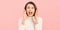 Energetic loud cute beautiful female opening mouth widely, putting hands to mouth, shouting standing isolated over pink background