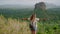 Energetic senior Asian woman with backpack reaches mountain peak, overlooks majestic Sigiriya Rock. Arms outstretched