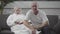 Energetic senior caucasian man watching sports match on TV. His calm blond wife sitting with husband and reading book