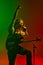 Energetic soulful man with dreadlocks, musician with electric guitar singing against gradient red green background in