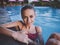 energetic woman in red swimsuit leaning on the tiles of the pool model transparent water naked shoulders