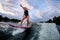 Energetic young woman stands on surf style wakeboard and balances on splashing wave