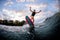 Energetic young woman stands on surf style wakeboard and ride down on wave