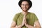 Energized and happy charismatic bearded man in glasses and hat holding palms together over chest in buddhist namaste