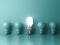 Energy saving light bulb , one glowing compact fluorescent lightbulb standing out from unlit incandescent bulbs on green