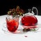 Energy splash red herbal tea in cup with transparent teapot, hawthorn, rosehip berry, dried leaves in contrast black and white.