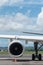 Engine and main landing gear when aircraft park on apron in the airport. The weather is good, blue sky and there are some cumulus