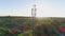 Engineer with gadget works on antenna communication tower and shows thumb up on background of city landscape in sunlight