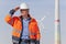 Engineer with hard hat and protective clothing in front of a windfarm looking for a bright future for green energy