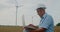 Engineer in hardhat uses laptop near wind turbines environmental