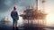 An engineer hat stands in front of an oil-producing industrial offshore platform. Factory worker with equipment for oil