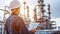 Engineer in helmet inspecting data at oil refinery with factory structures and dynamic sky