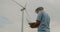 Engineer helmet and with a laptop his hands against backdrop of wind turbines.