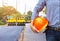 Engineer holding safety helmet at road construction site with roller compactor working asphalt road