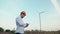 Engineer in orange hard hat at windmill power plant with tablet in hand on sky background. Slow motion. Wind Turbine