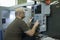 Engineer sitting in front of a control panel of CNC milling machine programming it