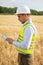 an engineer with a tablet in his hands stands in the middle of a green field, an agronomist in a field with wheat checks the