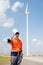 Engineer or technician worker stand in front of windmill or wind turbine and hold hardhat also look at camera in concept of