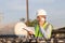 Engineer using smartphone with holding clipboard checklist in construction site, Foreman worker in hardhat and safety vest control