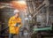 Engineer wearing yellow work clothes white hardhat and wear glove looking to the drilling machine while holding tablet.