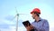 Engineer at windmill power plant with tablet in hand on sky background