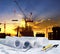 engineer working table plan, home model and writing tool equipment against building construction crane with evening dusky sky