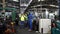 Engineers and employees walk inside the factory at break. Engineers and industrial workers are working on large machines.