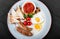 English breakfast - Fried eggs, beans, sausage, grilled tomatoes, mushrooms, toasted bread and sauce on plate on dark background