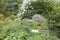 English garden with white rose pergola, flowering cottage plants .