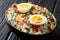 English green pea salad with boiled eggs, onions, bacon and cheddar cheese with cream sauce closeup in a bowl on the table.