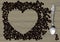 Engraved vintage color drawing of a heart shaped frame of coffee beans on wood textured background and retro spoon