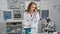 Engrossed young woman scientist taking notes while discussing research over smartphone in busy lab